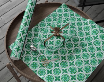 Puede incluir: Papel de regalo con estampado verde y blanco, un regalo envuelto con una cinta marrón y un rollo de papel a juego están sobre una mesa de madera. También hay tijeras doradas y cinta adhesiva sobre la mesa. El papel tiene un diseño circular.