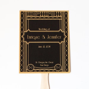 May include: A black and gold wedding fan with the text "Wedding of Enrique & Jennifer" and "June 21, 2014". The fan also includes the text "St. Gregory the Great, San Diego" and the initials "E&J".
