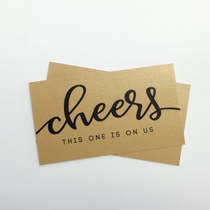 May include: Gold card with black text that reads "cheers this one is on us".