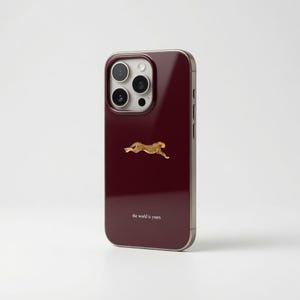 Puede incluir: Funda de teléfono burdeos con diseño de guepardo dorado. La funda tiene un acabado brillante y presenta el texto "the world is yours" en la parte inferior. La funda tiene un módulo de cámara con tres lentes.
