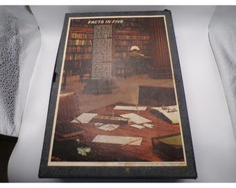 May include: A framed print titled "Facts in Five" depicts a library scene with a person reading at a desk. The image includes a table with papers, books, and eyeglasses. The frame is dark gray.