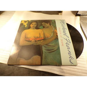 May include: A vinyl record album cover titled Michael Franks Objects of Desire. The cover features a painting of two figures holding a bowl of fruit, with a light blue vertical strip on the right side containing the artist and album name.