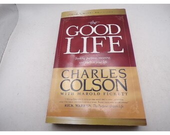 May include: A hardcover book titled "The Good Life" by Charles Colson. The book has a burgundy and tan cover with the title in large white letters. The subtitle reads "Seeking purpose, meaning, and truth in your life."