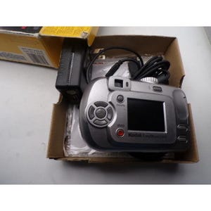 以下が含まれることがあります： 黒い画面、ボタン、レンズを備えたシルバーのKodak EasyShare C310デジタルカメラ。 カメラは、黒い充電器とケーブルが入ったオリジナルの段ボール箱に入っています。