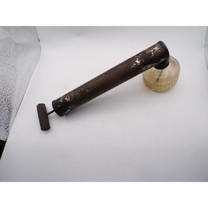 May include: An antique brown metal and glass perfume atomizer. The atomizer has a long, cylindrical body with a small handle and a round, ribbed glass bulb. The metal shows signs of age and wear.