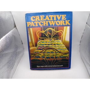 May include: A book titled "CREATIVE PATCHWORK" with a blue cover. The cover features a bed with a patchwork quilt and a gold-colored headboard. The text "New ways with a time-honoured craft" is at the bottom.