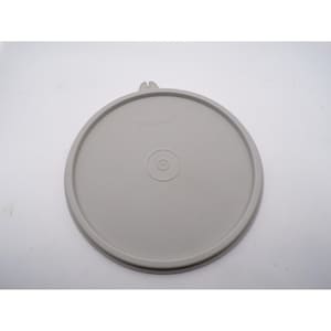 May include: A round, light gray Tupperware lid. The lid has a raised edge and a small tab on one side. The center of the lid features a circular indentation. The Tupperware logo is visible on the lid.