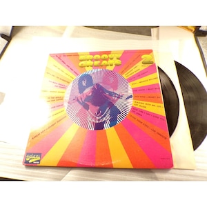 May include: A Groovy Greats double vinyl record album cover featuring a vibrant sunburst pattern in pink, orange, and yellow. The center displays a circular graphic with a stylized silhouette. The tracklist is printed in black text.