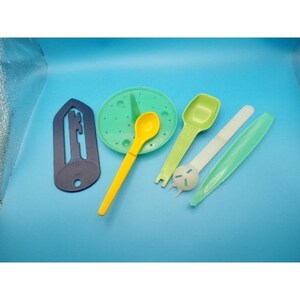 May include: Assortment of kitchen tools in various colors. Includes a yellow spoon, green scoop, white tool with a circular end, and a green serrated knife. Also, a dark blue utensil and a green perforated disc.