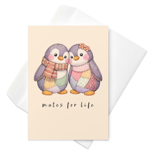 Puede incluir: Una tarjeta de felicitación con dos pingüinos de dibujos animados con cuerpos de retazos y pies naranjas. Uno lleva una bufanda, el otro un adorno floral. El texto "mates for life" está escrito debajo. La tarjeta está dentro de un sobre blanco.