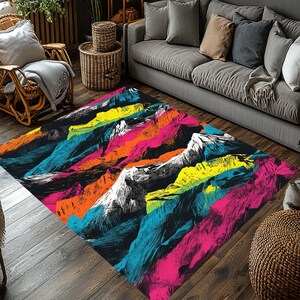 May include: A rectangular area rug with a vibrant mountain range design. The rug features a black background with colorful, stylized mountains in shades of pink, orange, yellow, blue, and white. The rug is placed on a wooden floor.