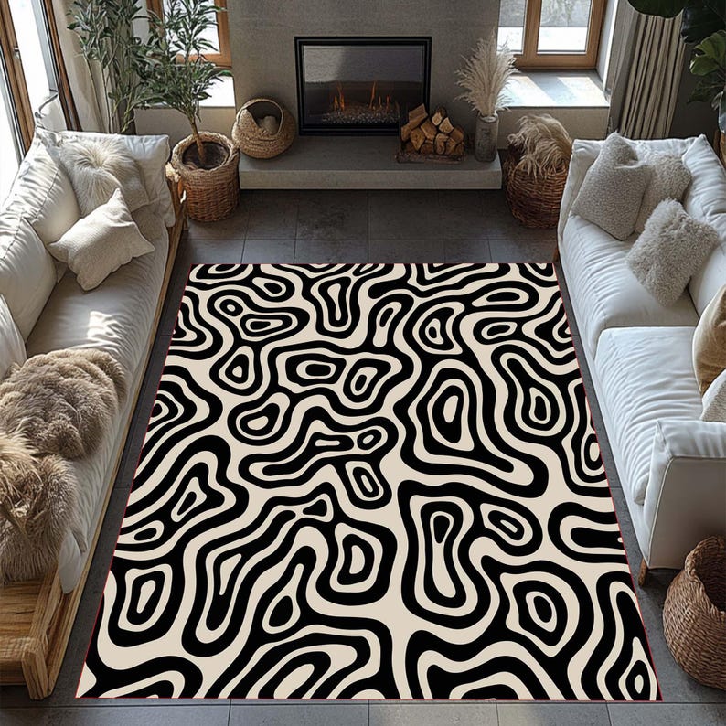 May include: A large rectangular area rug with a cream-colored background and a bold, black, abstract, swirling pattern. The rug is placed in a living room setting, with white sofas and a fireplace visible in the background.