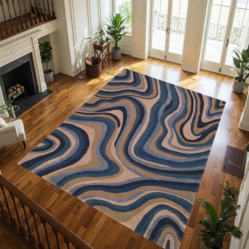 May include: A large area rug with a flowing, abstract design in shades of blue, tan, and brown. The rug's pattern resembles swirling water or a topographical map, adding a modern touch to the room. The rug is rectangular and covers a large portion of the wooden floor.