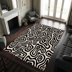 May include: A rectangular area rug with a black and cream abstract pattern. The rug features a repeating design of swirling, organic shapes. The rug is placed on a dark wood floor in a living room setting.