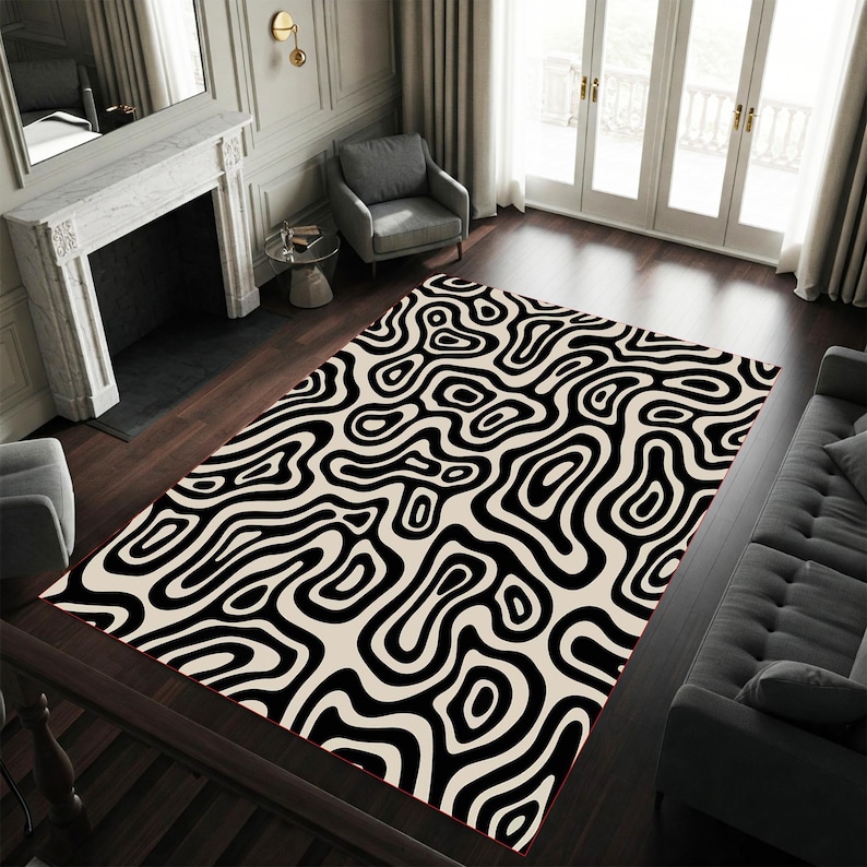 May include: A rectangular area rug with a black and cream abstract pattern. The rug features a repeating design of swirling, organic shapes. The rug is placed on a dark wood floor in a living room setting.