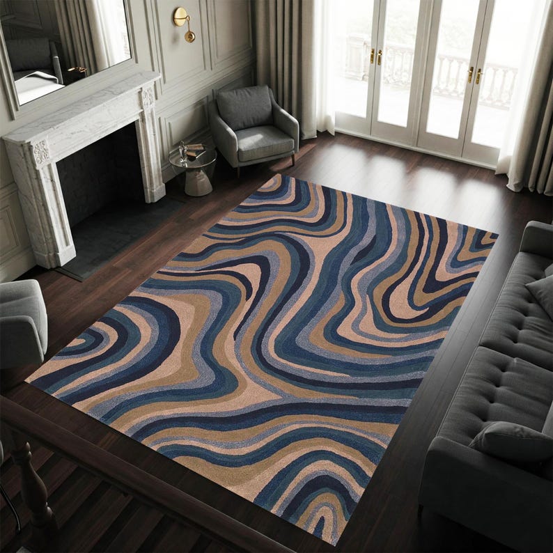 May include: A large area rug with a flowing, abstract design in shades of blue, tan, and beige. The rug's pattern resembles swirling waves or organic shapes, creating a visually dynamic floor covering. The rug is rectangular and appears to be made of a soft material.