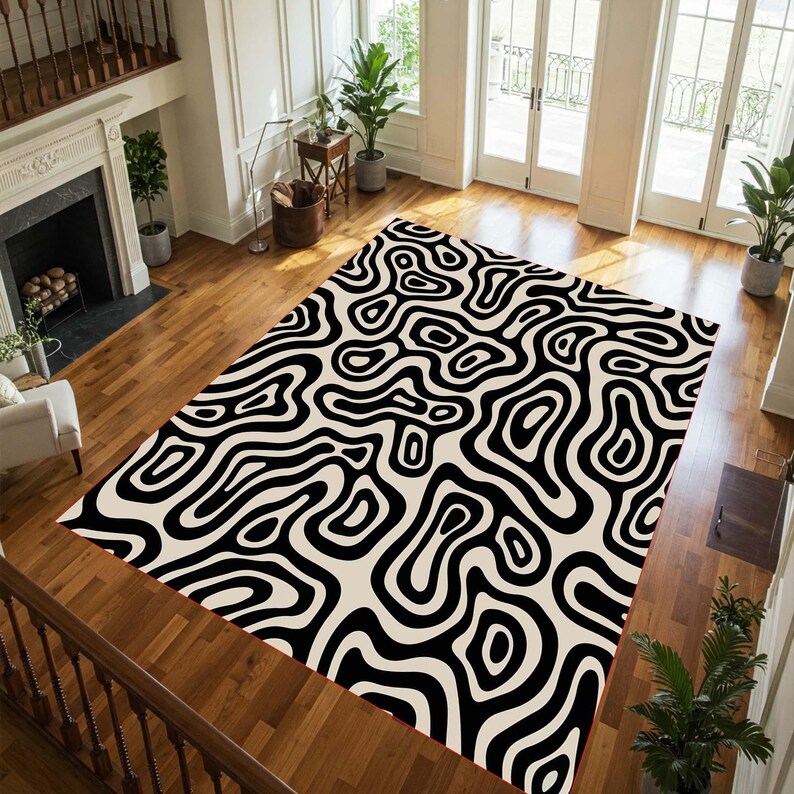 May include: A large area rug with a black and cream abstract pattern. The rug features a repeating design of swirling, organic shapes, creating a bold visual statement. The rug is placed on a hardwood floor in a well-lit room.