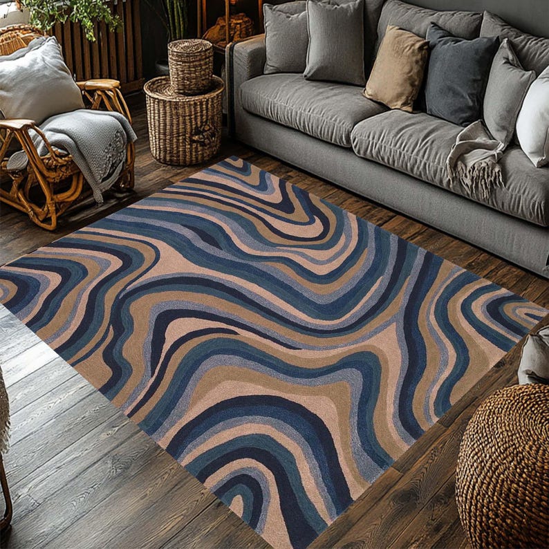 May include: A rectangular area rug with a swirling pattern in shades of blue, tan, and brown. The rug is placed on a wooden floor in a living room setting. The design resembles flowing water or geological formations.