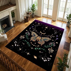 May include: A rectangular black area rug featuring a large butterfly with gold and teal wings. The rug has a celestial design with stars, moons, snakes, and floral elements. The top edge fades to a deep purple.