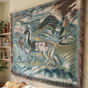 May include: A large tapestry with a horse design hangs above a brown leather sofa. The tapestry features a horse in shades of blue, green, and brown. The sofa is adorned with pillows and blankets in neutral tones, creating a cozy living room setting.