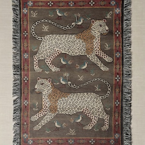 May include: A rectangular throw blanket with a repeating pattern of two leopards, birds, and floral motifs. The leopards are tan with brown spots, set against a gray background. The border is burgundy with fringe.