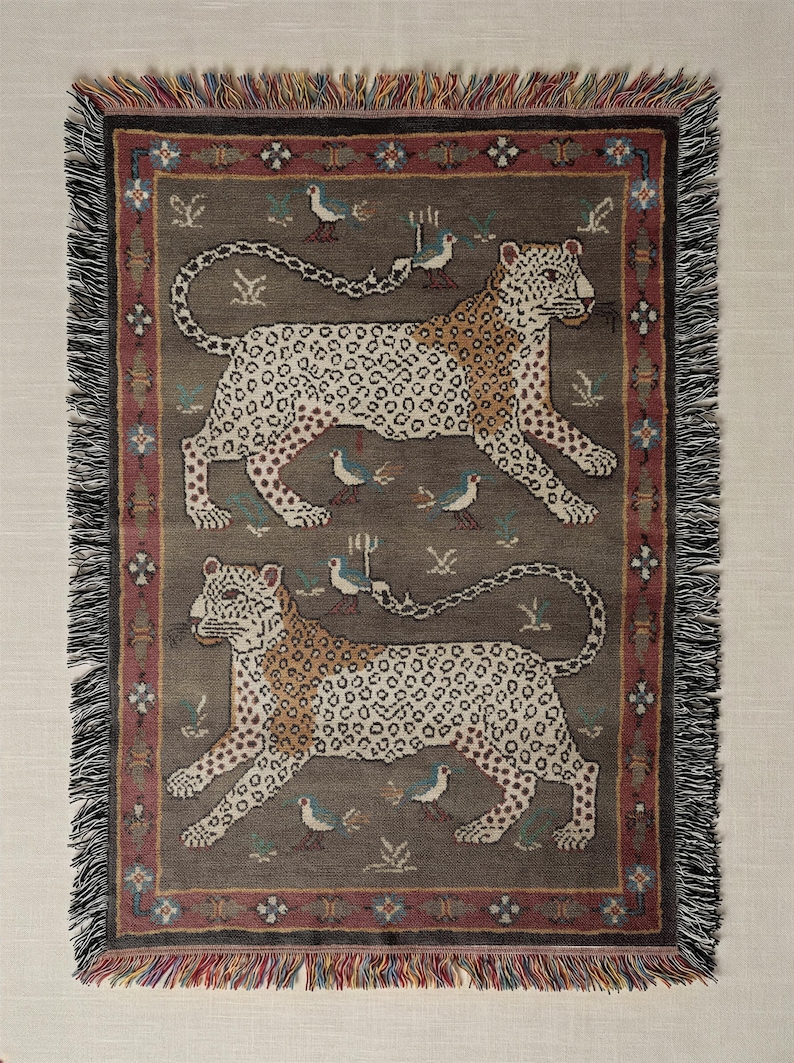 May include: A rectangular throw blanket with a repeating pattern of two leopards, birds, and floral motifs. The leopards are tan with brown spots, set against a gray background. The border is burgundy with fringe.