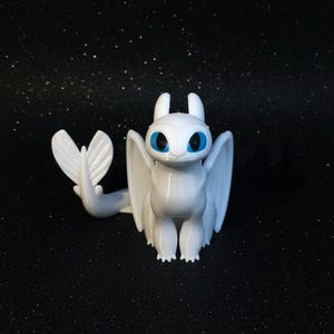 Puede incluir: Figura de dragón blanco con grandes alas, cola y ojos azules. El dragón está de pie con las alas extendidas. El fondo es negro con pequeños puntos brillantes.