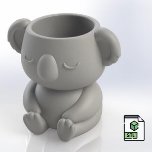 Puede incluir: Una maceta gris con forma de koala con una gran abertura para plantas. El koala está sentado con las piernas cruzadas y los ojos cerrados. La maceta tiene orejas redondeadas y una nariz pequeña. También hay un icono de archivo STL.