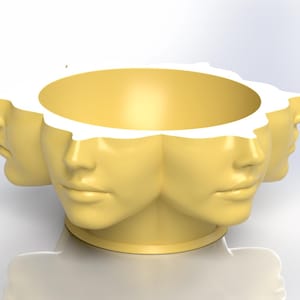 May include: A yellow decorative planter featuring multiple human faces around the rim. The faces are smooth and stylized, with a neutral expression. The planter has a circular opening and a pedestal base.
