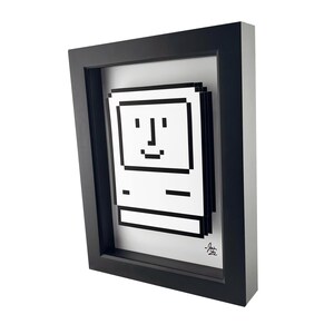 May include: A black framed print of a pixelated image of an Apple Macintosh computer with a smiling face. The print is signed "J.an 22".