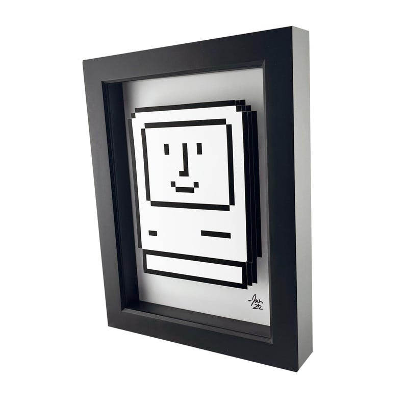 May include: A black framed print of a pixelated image of an Apple Macintosh computer with a smiling face. The print is signed "J.an 22".