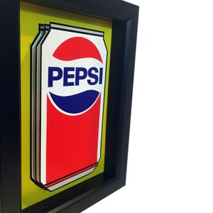May include: A framed illustration of a red and blue Pepsi can on a yellow background.