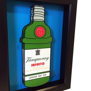 Puede incluir: Una ilustraci&oacute;n enmarcada de una botella de ginebra Tanqueray verde con un sello rojo y el texto "IMPORTED" y "LONDON DRY GIN".