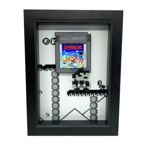 May include: A framed 3D pixel art piece featuring a Super Mario Land Game Boy cartridge and a pixelated Mario character. The background is a pixelated level from the game.