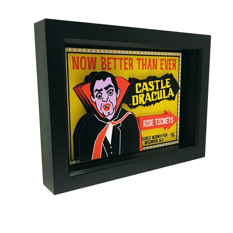 May include: A framed illustration of a vintage amusement park ride advertisement. The illustration features a vampire with a red cape and the text "Now Better Than Ever Castle Dracula Ride Tickets."