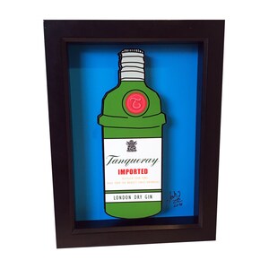 Puede incluir: Una ilustraci&oacute;n enmarcada de una botella verde de ginebra Tanqueray London Dry. La botella est&aacute; en un estilo 3D, con la etiqueta y la tapa de la botella saliendo del marco. El fondo es de color azul brillante.