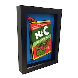 Puede incluir: Una ilustración enmarcada de una caja de jugo Hi-C Ecto Cooler con el personaje de los Cazafantasmas Slimer. La caja es verde, roja y amarilla con el texto "Hi-C Ecto Cooler" y "100% U.S. RDA of Vitamin C Per Serving".