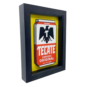 May include: A framed print of a Tecate beer can. The can is red, yellow, and black with the words "Tecate Cerveza Original 12 Fl. Oz. Lager" printed on it.