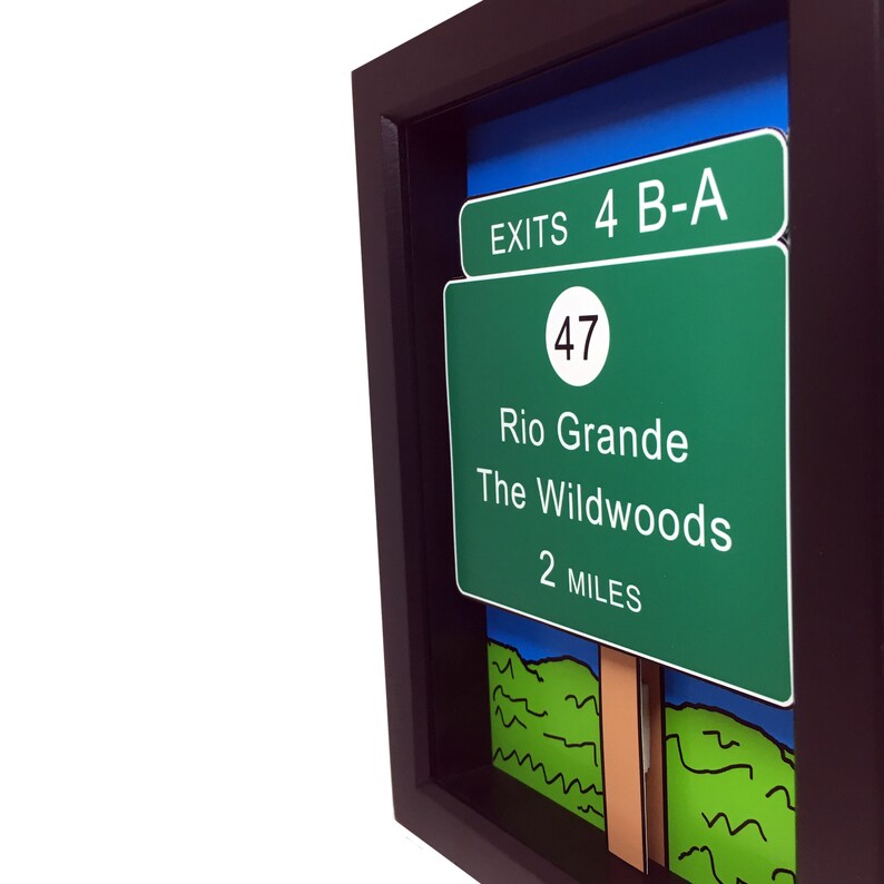 May include: A framed green and white highway sign with the text "EXITS 4 B-A", "47", "Rio Grande", "The Wildwoods", and "2 MILES".