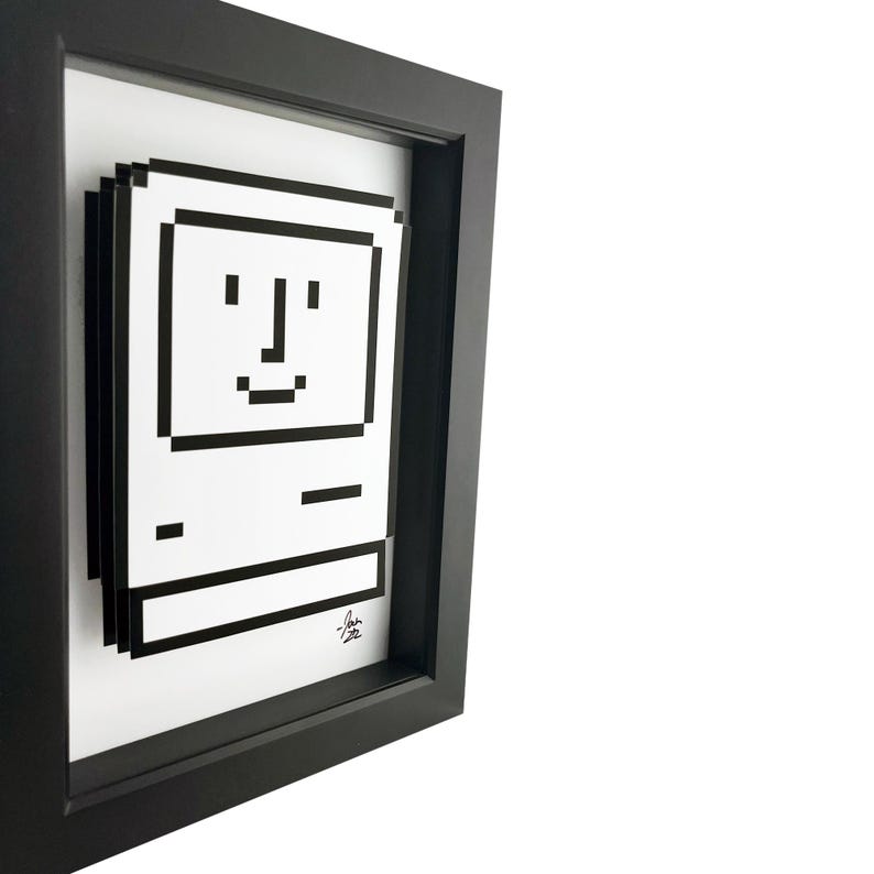 May include: A black and white pixel art print of a vintage Apple computer in a black frame. The computer has a smiling face.