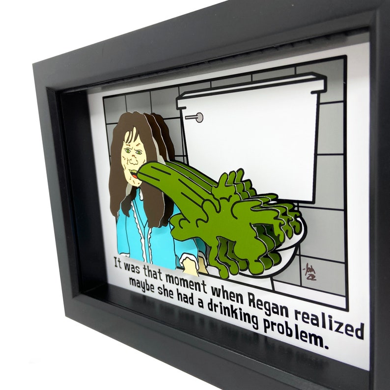 May include: A framed illustration of a woman vomiting green goo into a toilet bowl. The caption reads "It was that moment when Regan realized maybe she had a drinking problem."