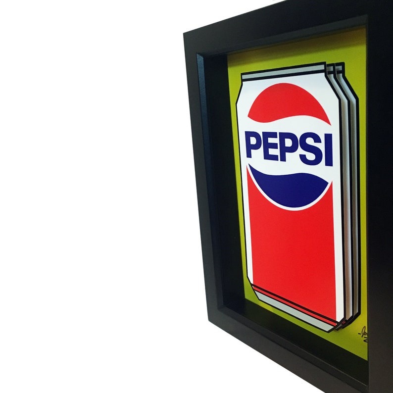 May include: A framed print of a Pepsi can with a yellow background. The can is red and white with the Pepsi logo in blue.