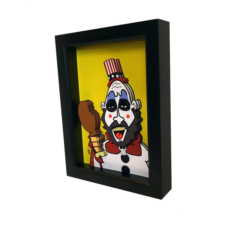 May include: A framed 3D paper art piece depicting a cartoon character with a red, white, and blue hat, a white beard, and a red bow tie. The character is holding a brown chicken leg in their right hand. The background is yellow.
