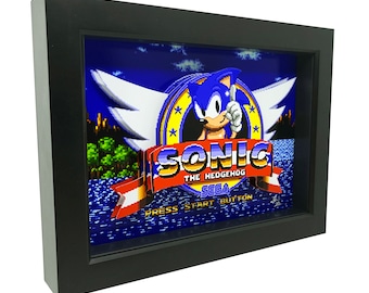 May include: A black framed 3D picture of Sonic the Hedgehog. The image is a pixelated recreation of the classic video game character. The image features Sonic in his signature blue and red colors, with his signature red shoes and white gloves. The image also features the words "Sonic the Hedgehog" and "SEGA" in a red banner.