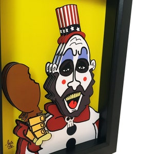 May include: A framed papercraft illustration of a cartoon character with a red, white, and blue hat, a red bow tie, and a white and blue clown costume. The character is holding a brown chicken leg. The background is yellow.