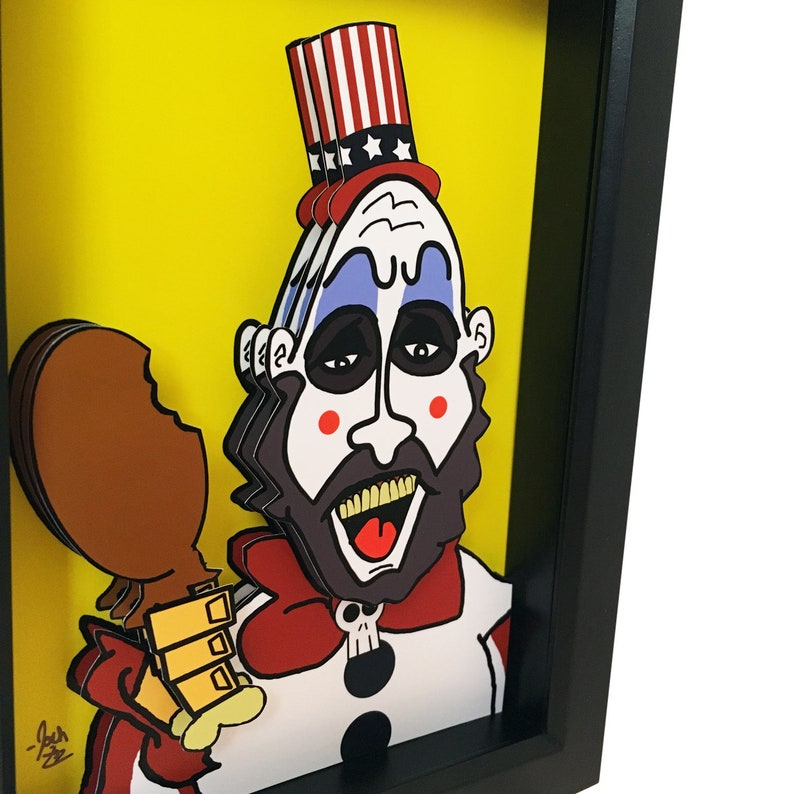 May include: A framed papercraft illustration of a cartoon character with a red, white, and blue hat, a red bow tie, and a white and blue clown costume. The character is holding a brown chicken leg. The background is yellow.