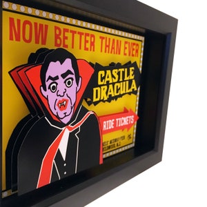 May include: A framed illustration of a vampire with a red cape and the text "NOW BETTER THAN EVER CASTLE DRACULA RIDE TICKETS" on a yellow background.