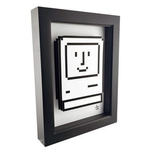 May include: A black framed print of a pixelated computer with a smiling face. The print is in a black frame and has a white background.