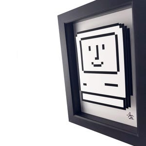 May include: A black framed print of a pixelated computer with a smiling face. The print is signed "Josh 22".