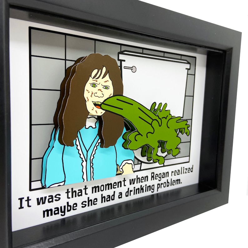 May include: A framed illustration of a girl with brown hair vomiting green goo into a toilet. The text below reads "It was that moment when Regan realized maybe she had a drinking problem."